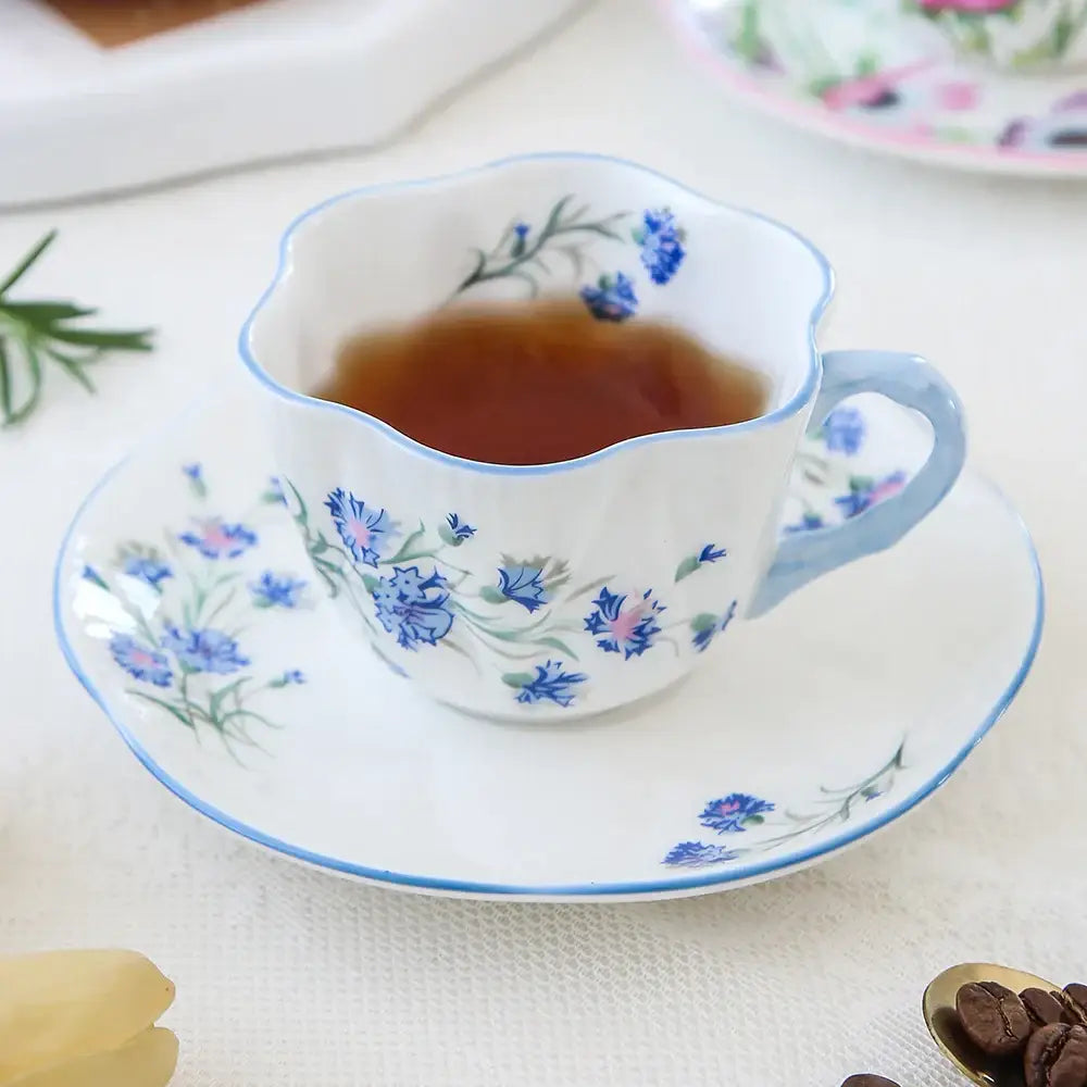 A delicate white porcelain coffee cup with scalloped rim and blue floral pattern filled with amber tea from decorbites bone saucer set