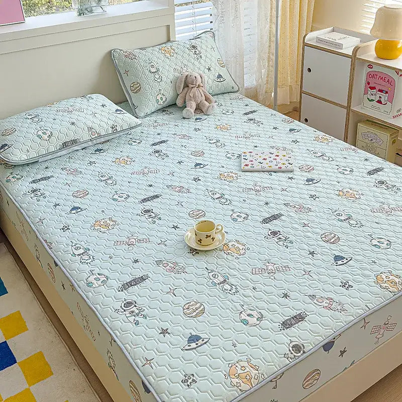 Light blue quilted latex bed pad with pastel space-themed pattern in fitted sheet set for bedroom use