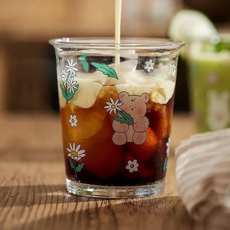 A clear bear rabbit glass tea tumbler with pastel floral design filled with iced coffee for kitchen use