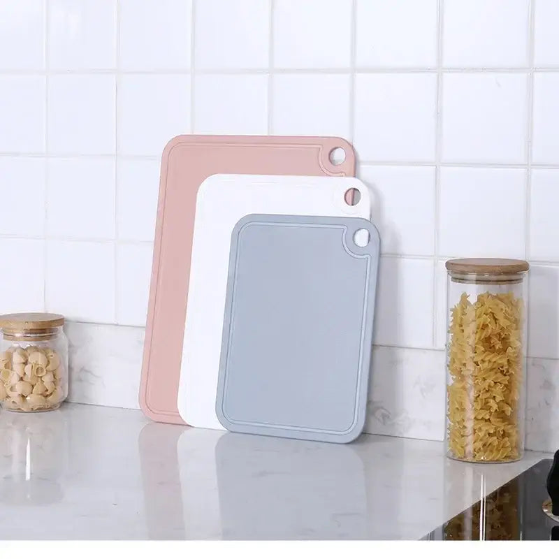 Set of three pastel-colored silicone kitchen cutting boards in pink white and gray with hanging holes from decorbites cutting board set