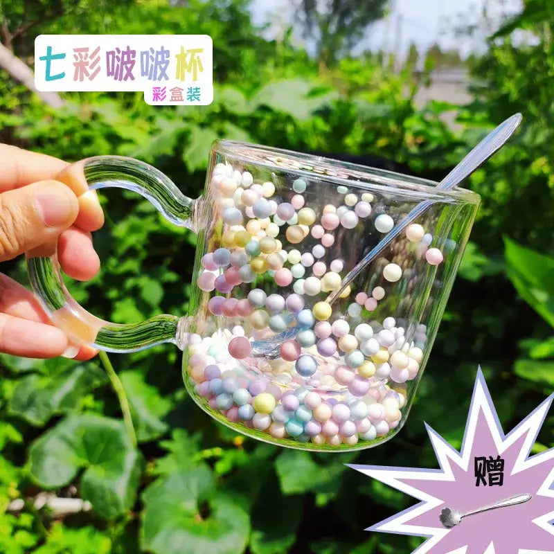 Clear glass cup filled with pastel heart bubble quicksand beads with spoon featuring double wall design for dining room use