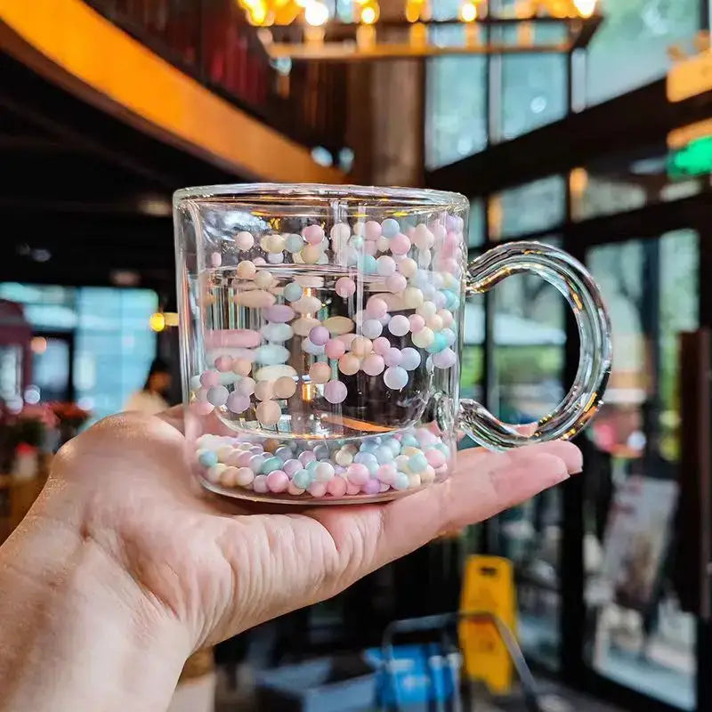 A clear double wall glass cup filled with pastel-colored heart bubble quicksand beads for dining room use