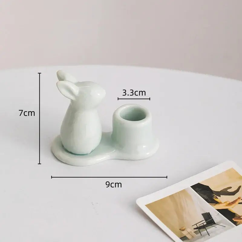 A delicate light green ceramic bunny rabbit candle holder shaped like a sitting rabbit with an integrated cup
