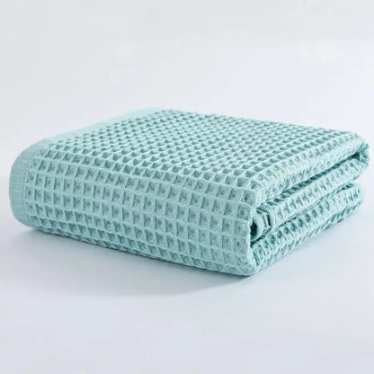 A neatly folded mint green decorbites cotton waffle bath towel with a textured grid pattern for bathroom use