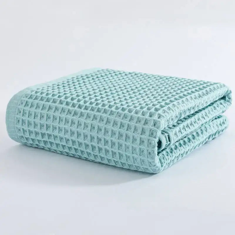 A neatly folded mint green decorbites cotton waffle bath towel with a textured grid pattern for bathroom use