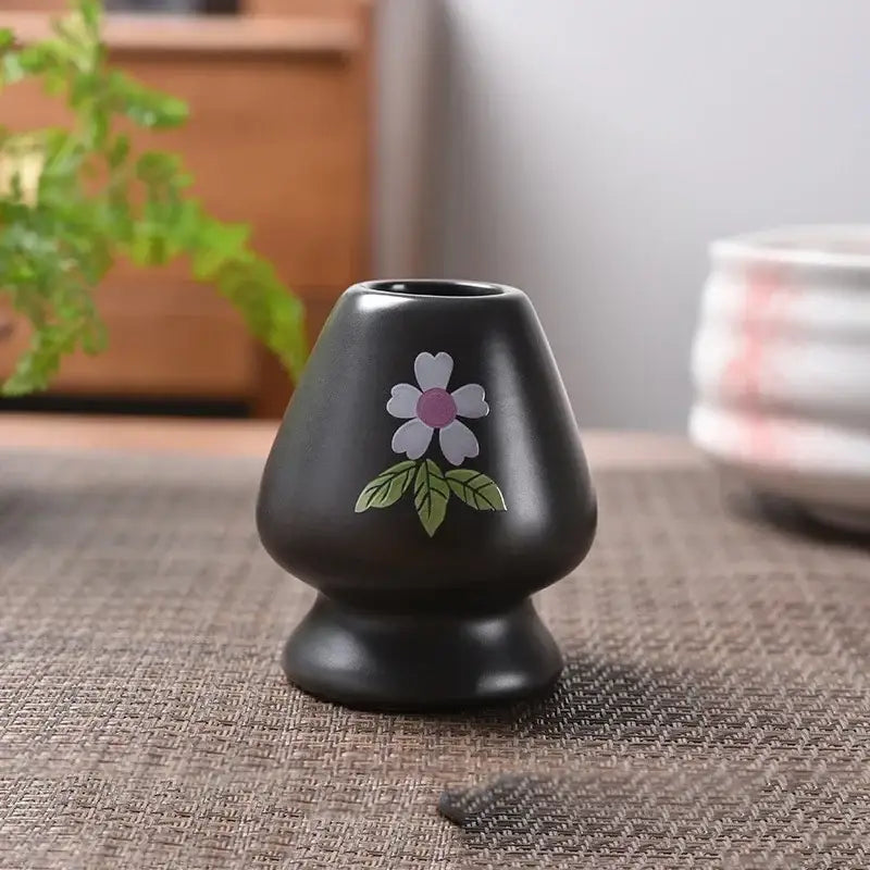 Black ceramic tea scoop with hand-painted white flower and pink center for pastel pink and yellow matcha whisk stand set