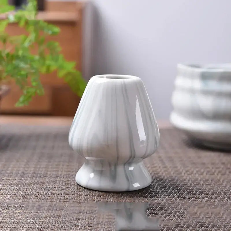 A small glossy white ceramic matcha whisk stand with subtle gray marbling and flared top for tea bowl holder use