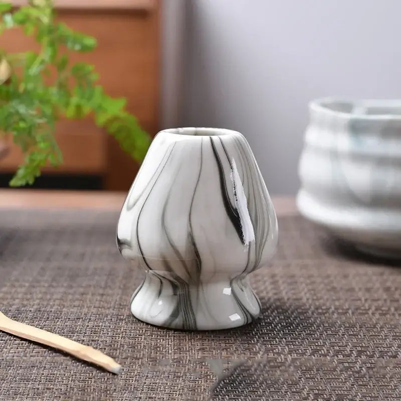 A small glossy ceramic matcha whisk stand with a white base and black marble swirls for tea bowl holder use
