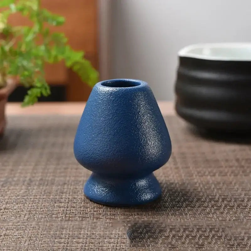 A matte blue ceramic tea bowl holder with a textured tapered body and flared base for matcha whisk stand use