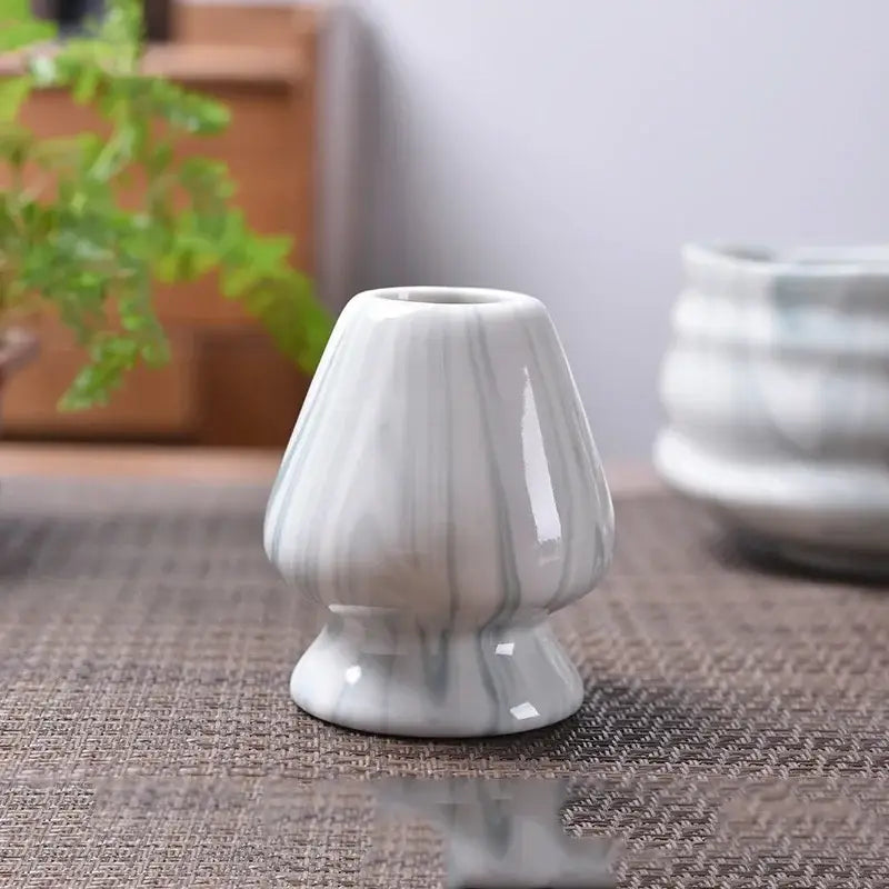 A sleek white ceramic matcha whisk stand with elegant gray marbling and fluted tapered design for tea bowl holder