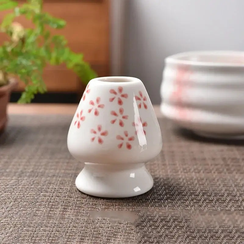 White ceramic matcha whisk stand shaped like a miniature mushroom with delicate pink floral patterns for tea bowl holder