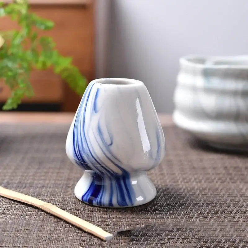 Pastel pink and yellow ceramic matcha whisk stand with white ceramic tea bowl holder featuring blue marbled patterns