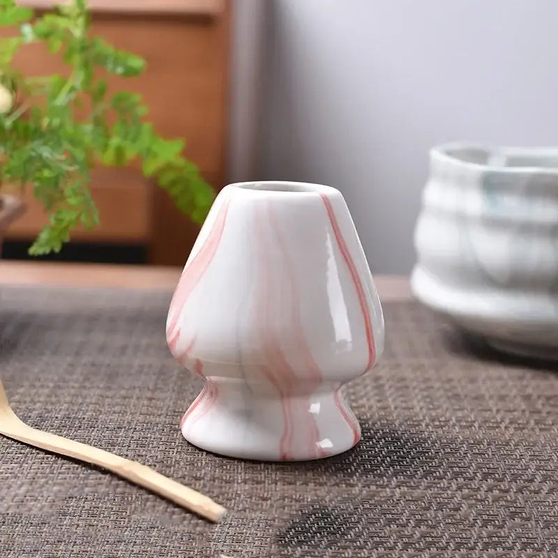 A white ceramic tea scoop with pink marble swirls and glossy finish for a pastel pink and yellow matcha whisk stand