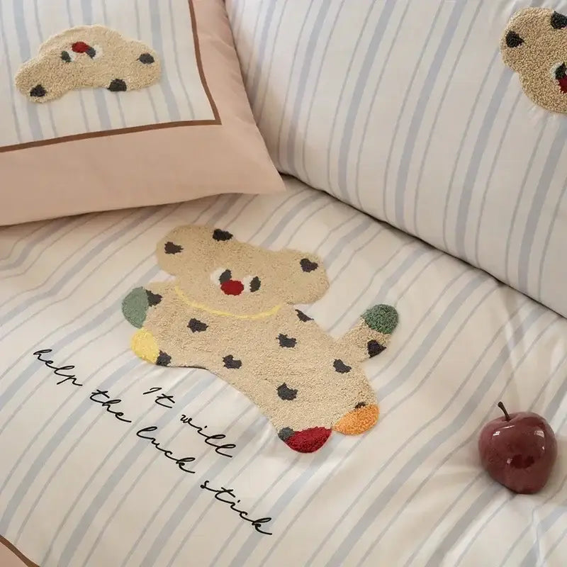 A beige plush teddy bear rug with black spots rests on pastel pink and gray decorbites cotton embroidered bedding set