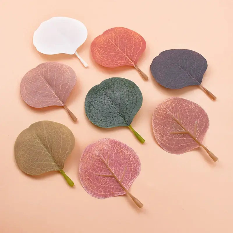 A collection of delicate pastel pink and green silk leaf artificial plants and translucent leaf-shaped paper clips for home decor