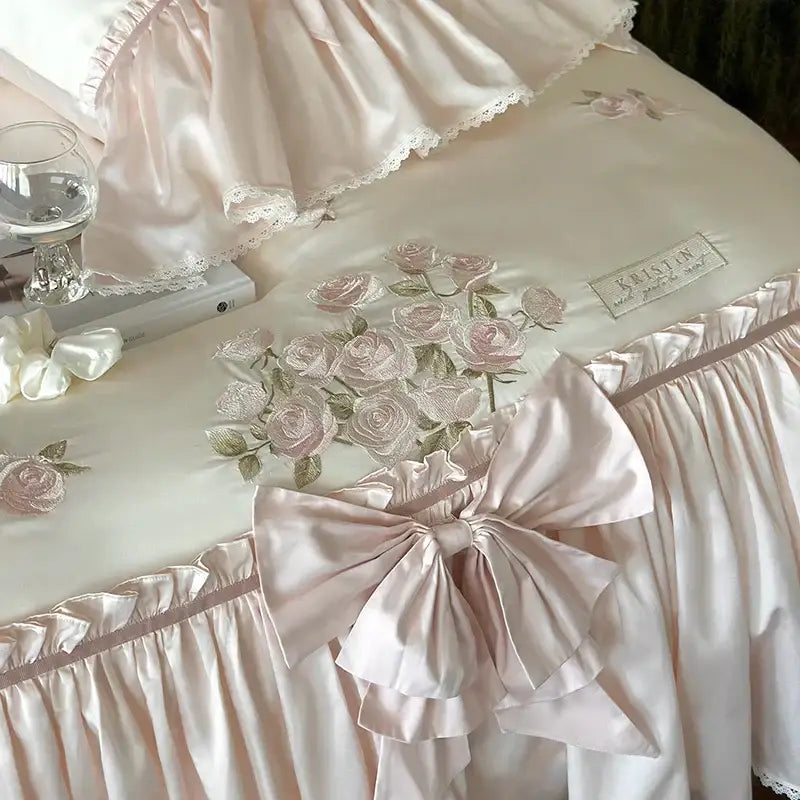 Pastel pink lyocell bedding set featuring a delicate satin bed skirt with ruffle flower embroidery and matching bow