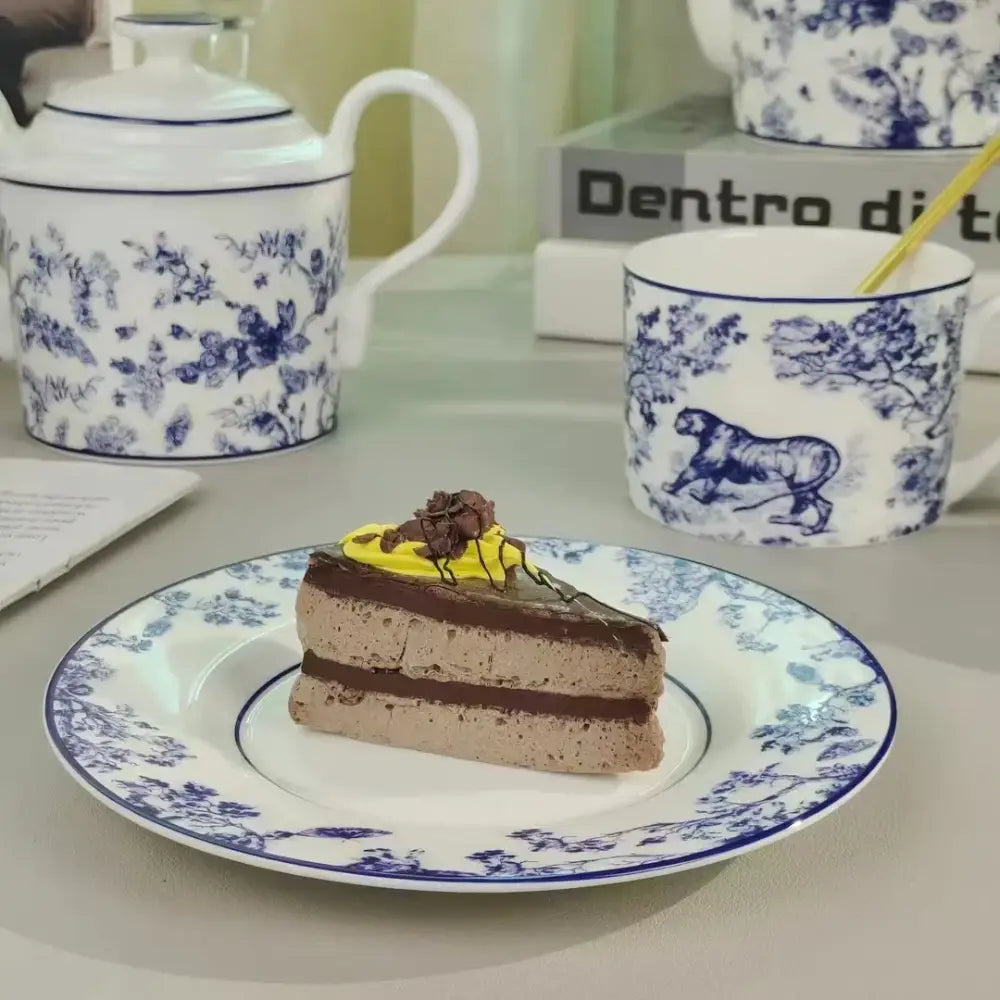 A slice of chocolate layered cake with yellow frosting on a white blue floral plate from decorbites jungle lion bone tea set decor