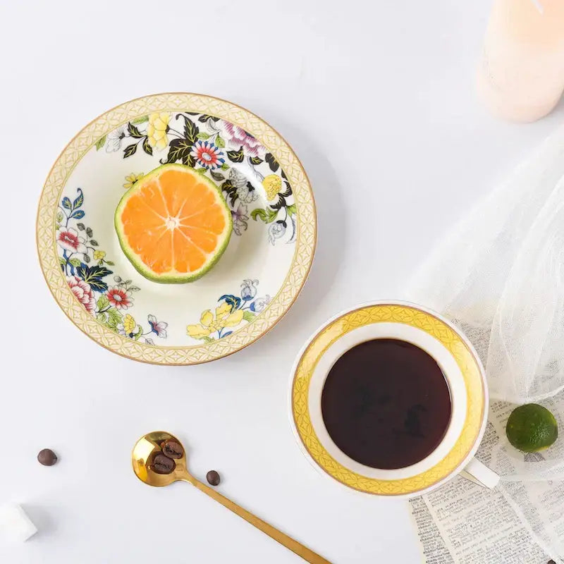 A delicate porcelain plate with vibrant floral pattern and gold-trimmed edges holding a halved orange for tea time
