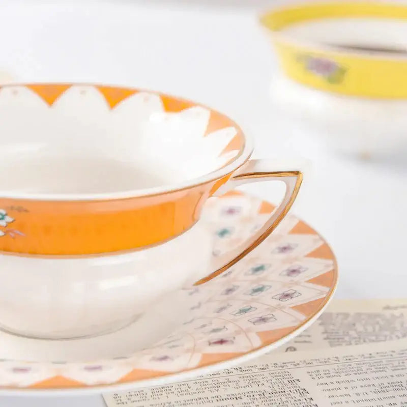 A delicate white bone china flower coffee cup with orange rim and gold handle resting on matching coffee cup saucers for tea time