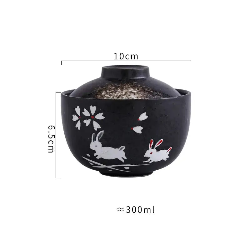 Black ceramic stew pot bowl with lid featuring white rabbit and cherry blossom decals accented with red dots