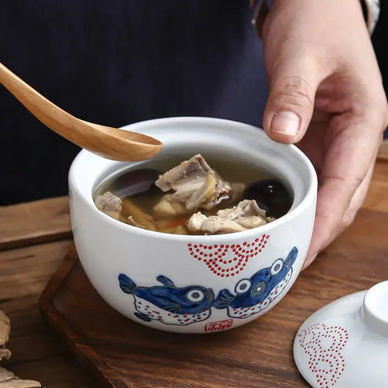 Patterned white and blue ceramic stew pot bowl with fish and red dot design holding steaming chicken herb broth