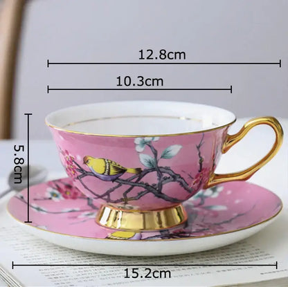 Pink porcelain teacup and saucer set with gold trim featuring a painted cartoon bird pattern for dining room use