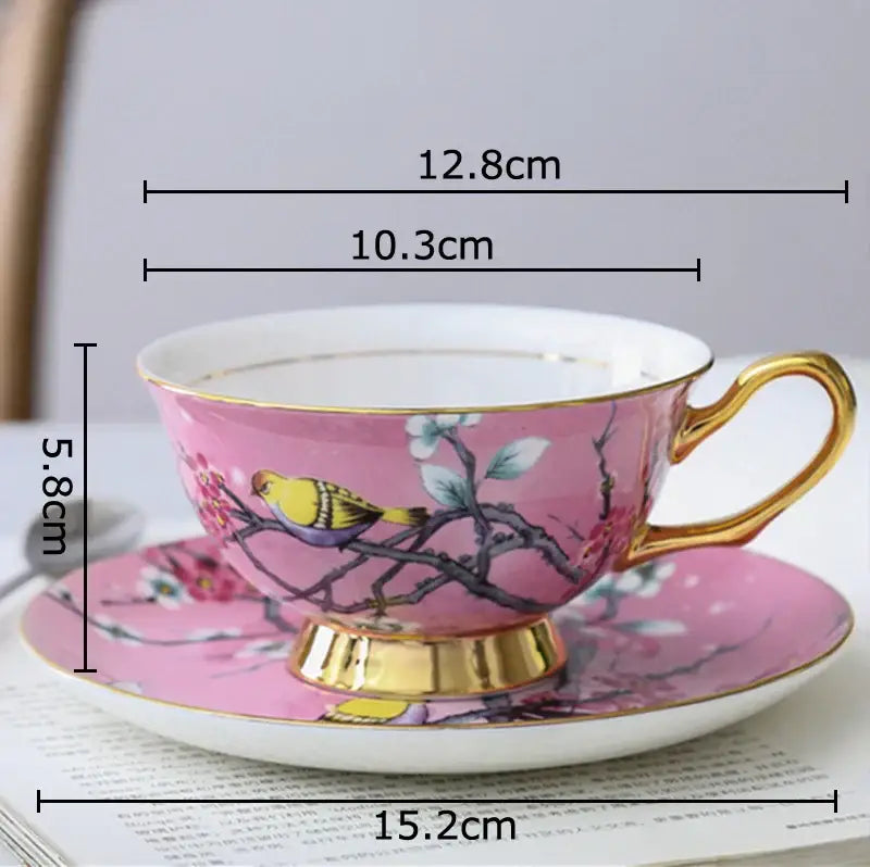 Pink porcelain teacup and saucer set with gold trim featuring a painted cartoon bird pattern for dining room use