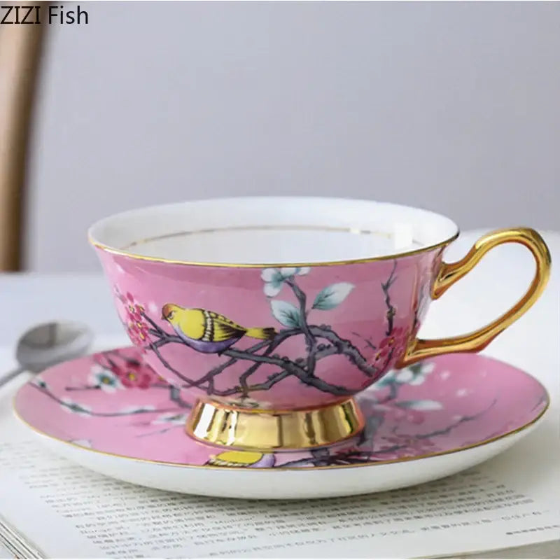 Pink porcelain teacup with gold trim and cartoon bird pattern on cherry blossom branch resting on matching saucer