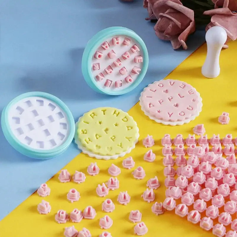 Pastel-colored pink and yellow plastic decorbites cookie stamps set with circular letter and word designs for baking