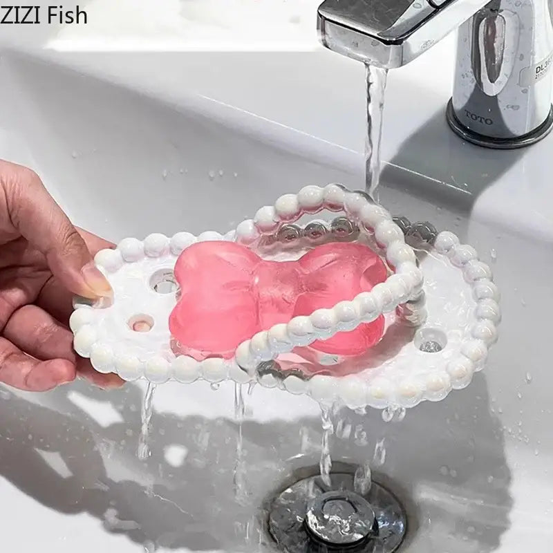 Pink translucent bow-shaped soap dish drainage rack with white beaded edge and silver metallic accents for bathroom use