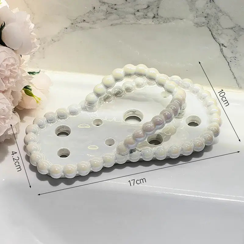 White ceramic soap dish drainage rack with beaded edge and circular cutouts shaped like infinity symbol for bathroom use