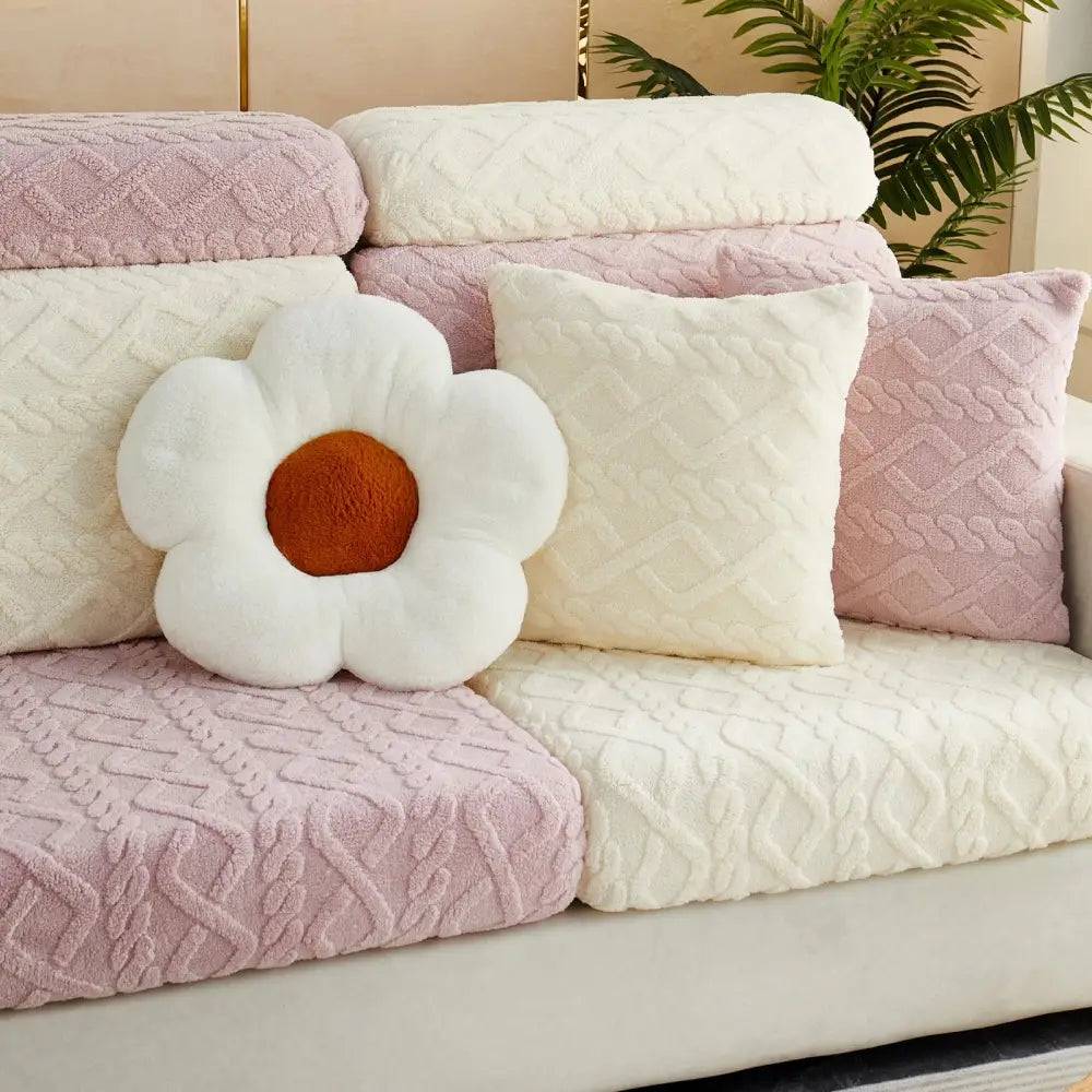 A plush white flower pillow with brown center on a pink and cream quilted velvet sofa cover seat protector