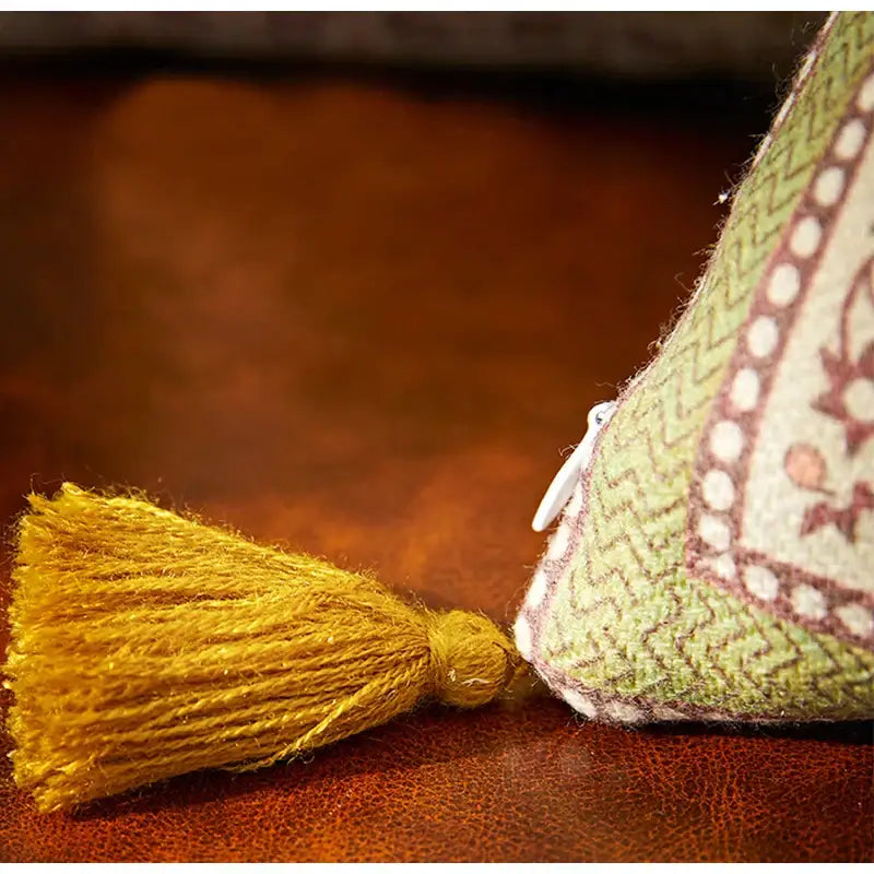 A mustard-yellow tassel beside a green and cream pouch complements the pink and green datura flowers print cushion cover