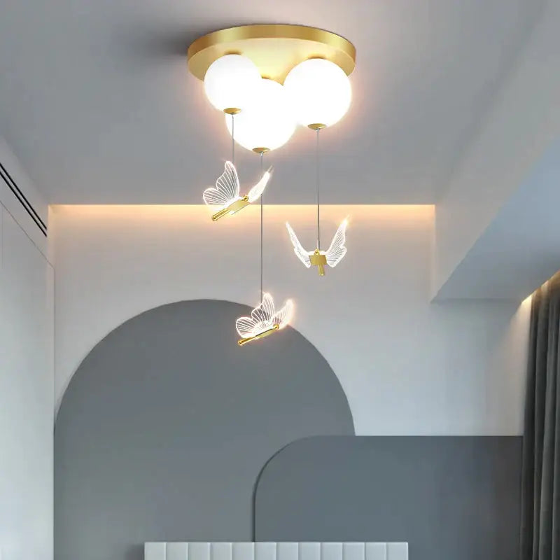 Gold-toned decorbites butterfly ball ceiling lamp with three glowing spheres and pink and white butterfly ornaments for bedroom decor