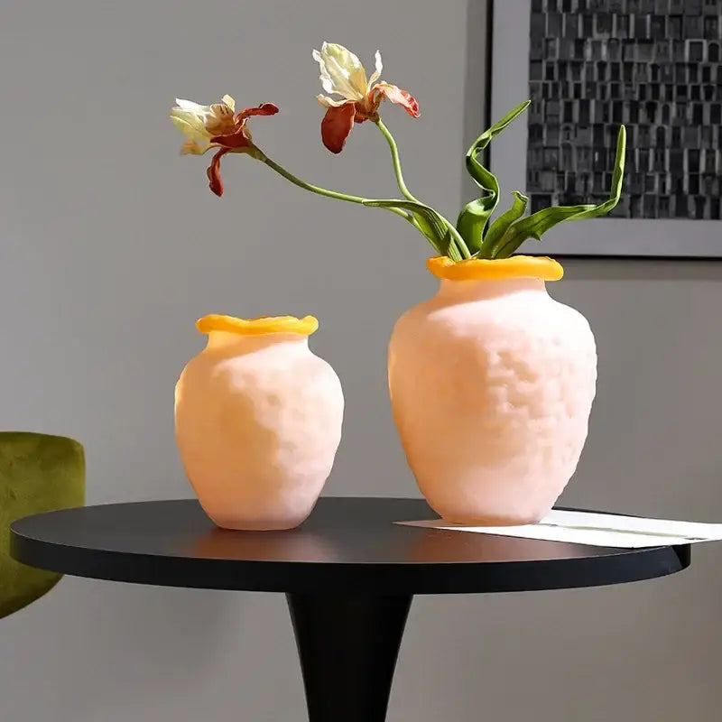 Two blush pink frosted glass vases with bright yellow rims holding flowers for colorful frosted decorbites decor