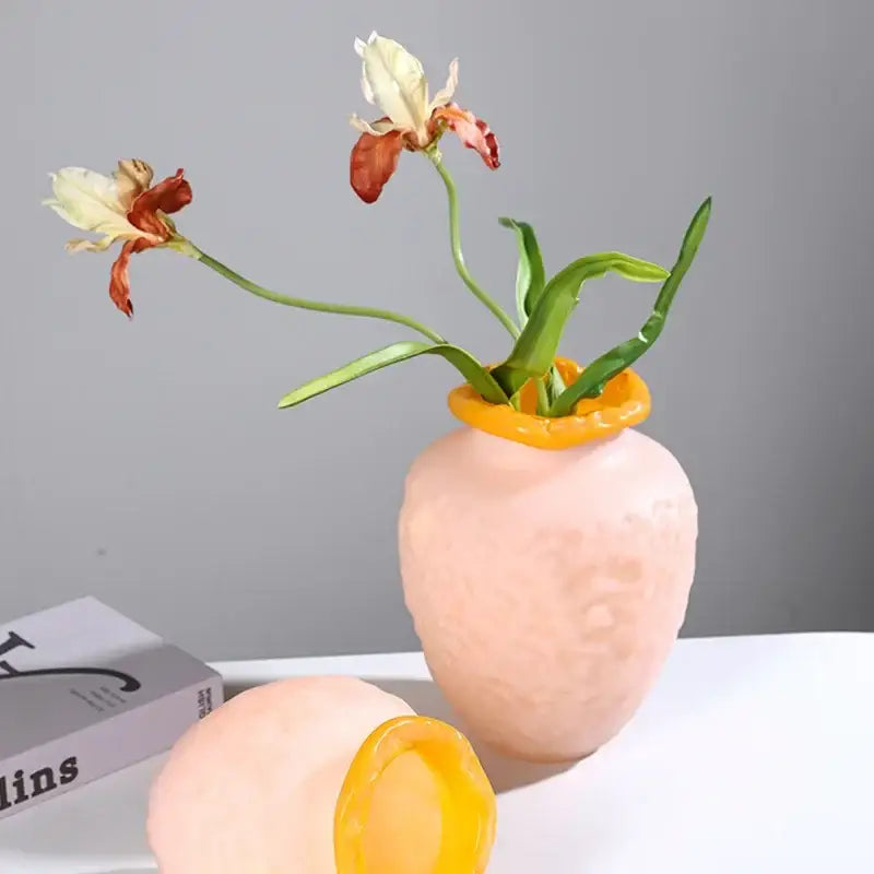 A blush pink and yellow textured colorful frosted glass vase with wilted white and orange flowers for living room decor