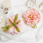 Pink big peony headwear artificial flowers with layered petals and green leaves displayed on lace surface for wedding decoration