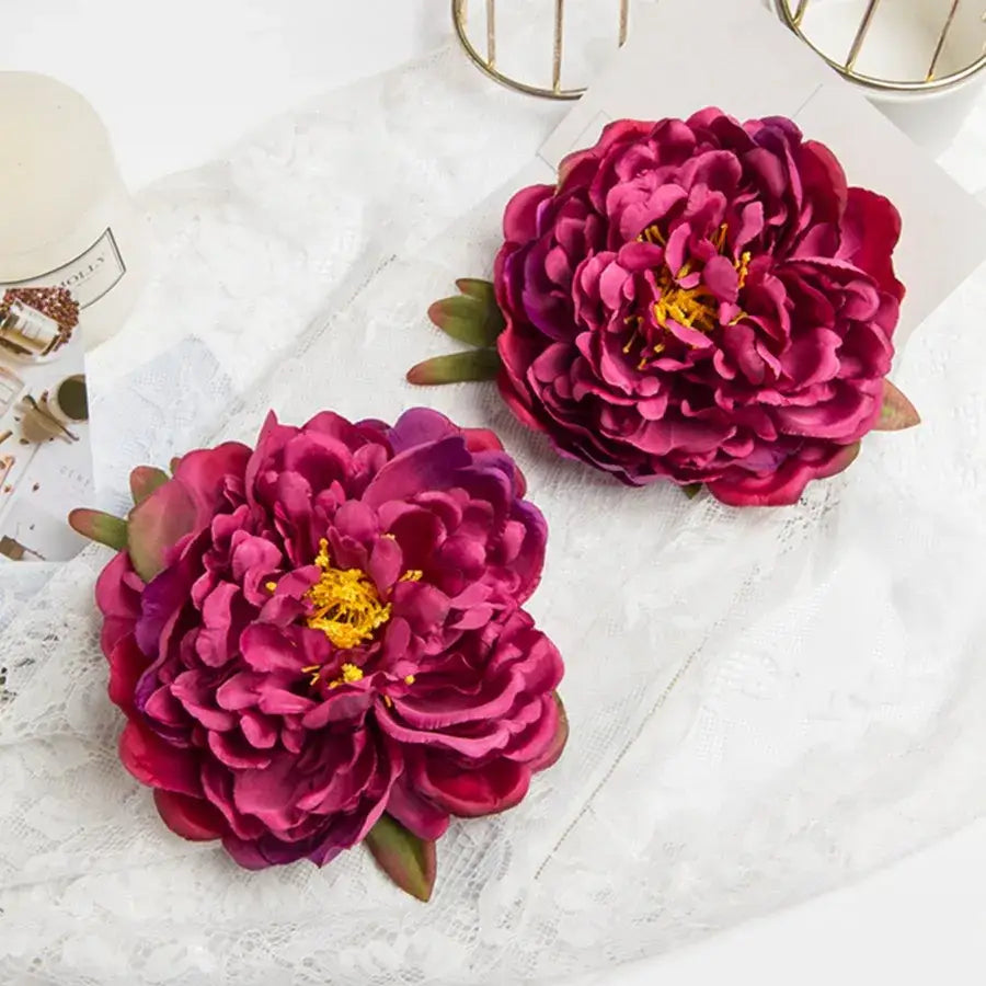 Two deep magenta artificial flowers featuring big peony headwear with layered petals and green leaf accents for weddings