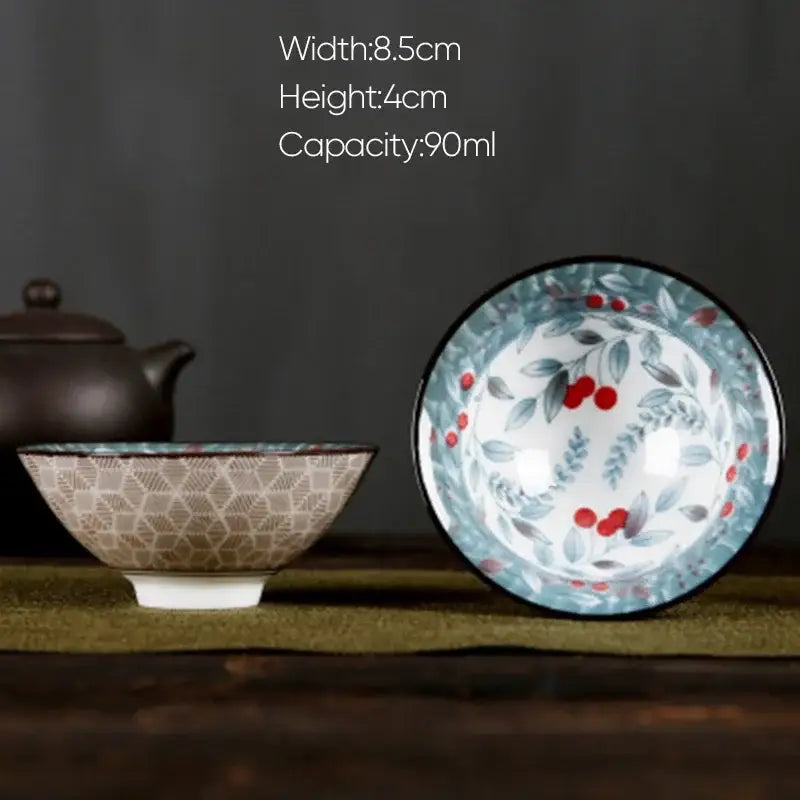 A white porcelain hand-painted bowl with red berries green leaves black rim on a decorbites blue background