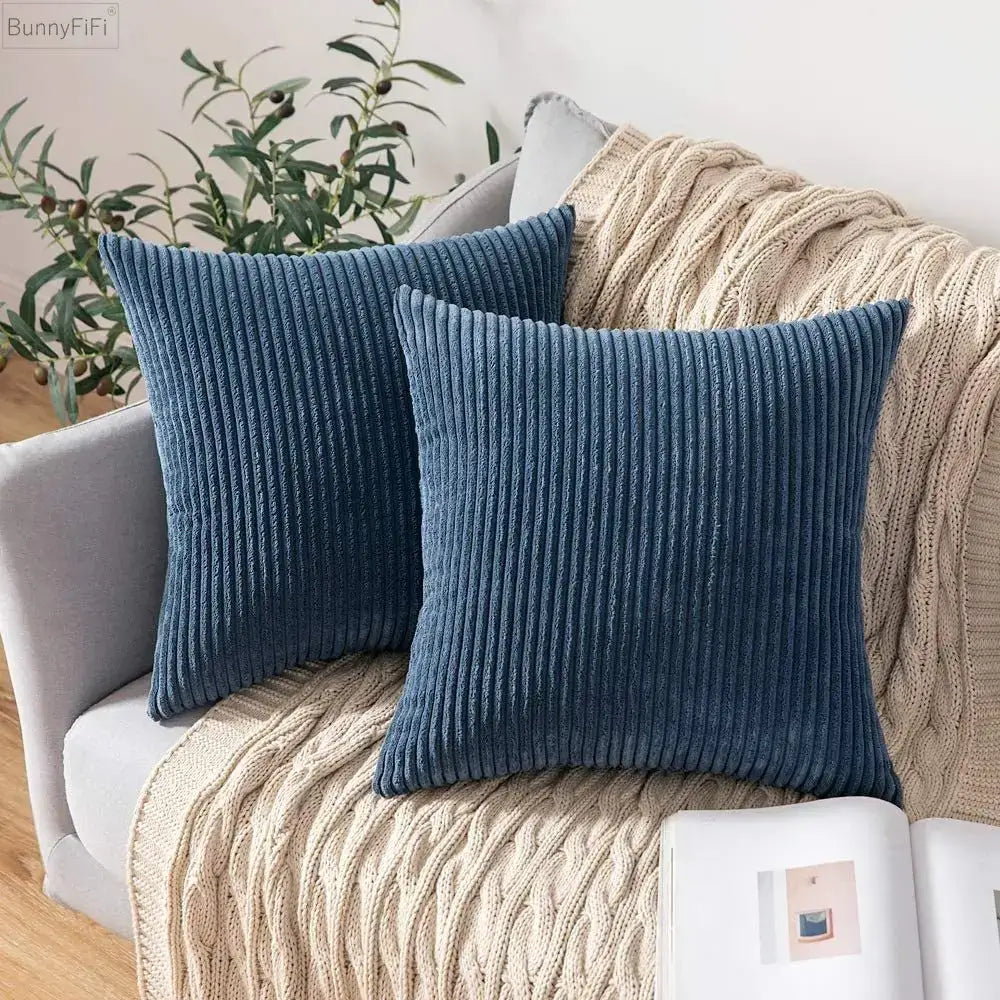 Two navy blue ribbed decorbites corduroy pillow covers resting on a couch with a beige knitted blanket in living room decor