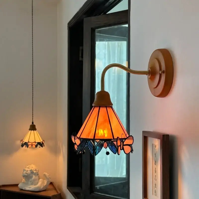 A warm amber glass led wall sconce with brass arm wooden mount and intricate butterfly decorbites glass led design