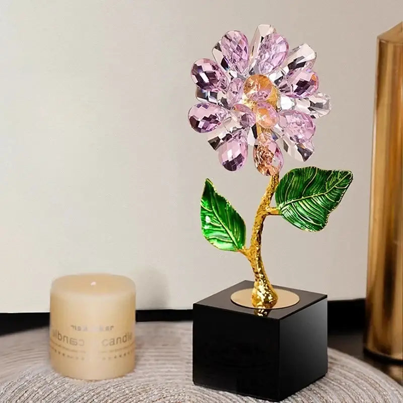 A sparkling pink and gold crystal sunflower metal sculpture with green leaves on a black base for home decor