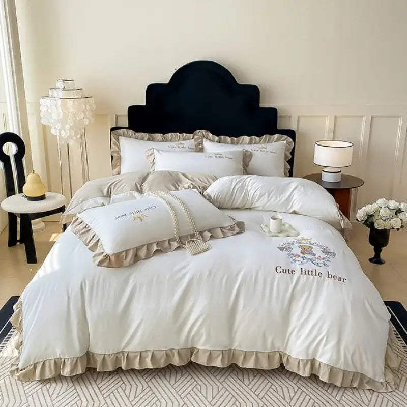 Cream-colored cotton bed skirt set with ruffled edges and embroidered cute little bear design on the duvet