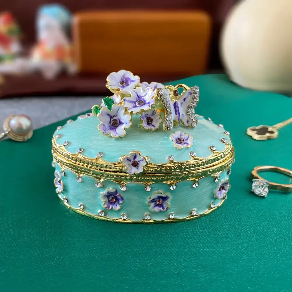 A mint green enamel jewelry trinket box with gold trim and floral butterfly design for elegant storage case use