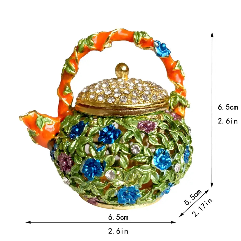 A vibrant teapot-shaped jewelry trinket box with gold crystal lid, orange handle, green leaves, and blue flowers storage case