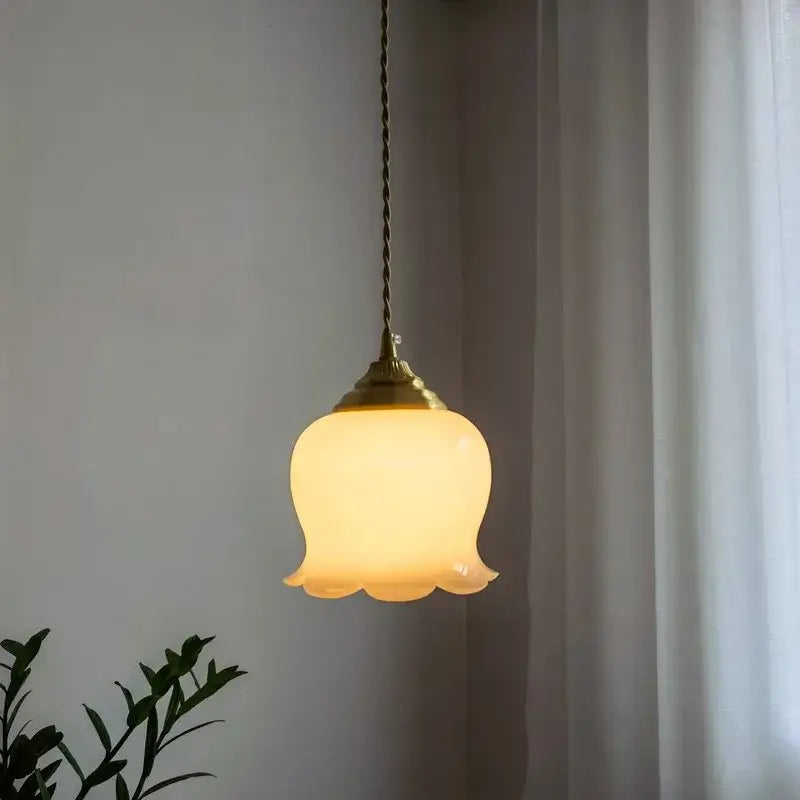 A warm glowing glass copper led pendant light with a brass top and flower-shaped off-white shade for kitchen decor
