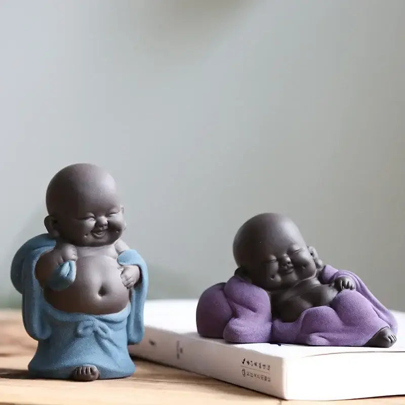 Two ceramic smiling baby bodhisattva figurines in blue and purple as part of a maitreya buddha statue tea sculpture