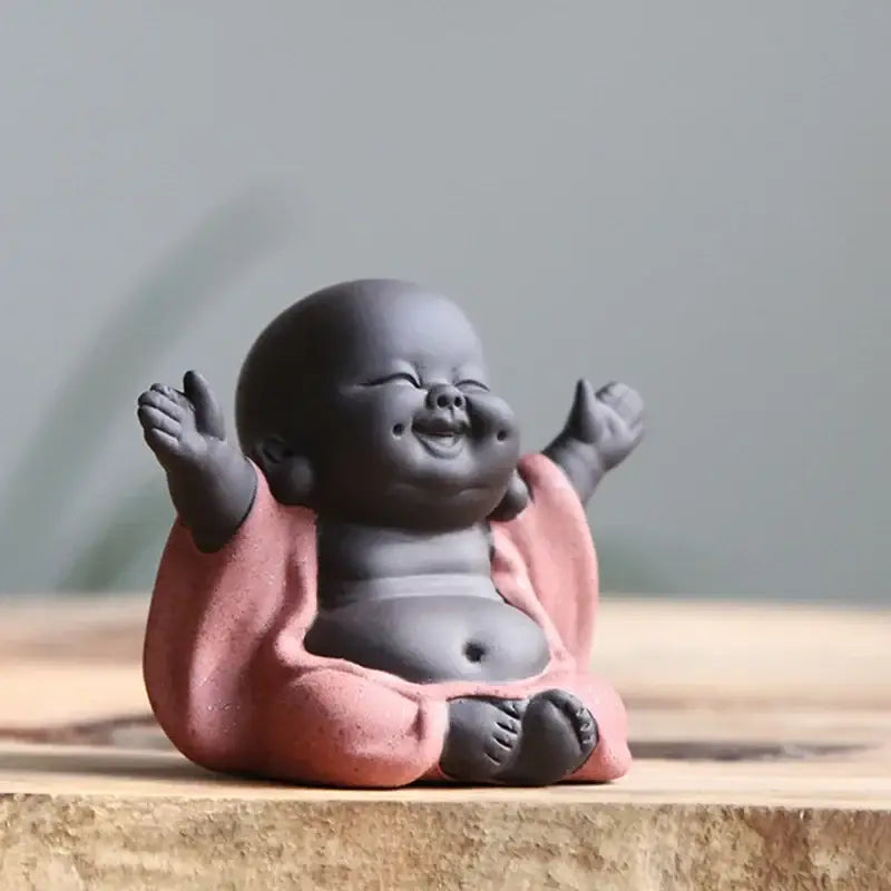 A smiling ceramic maitreya buddha statue with a matte gray body and pink robe for living room tea sculpture use