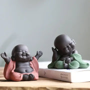 Two ceramic maitreya buddha statue tea sculptures in pink and green robes with smooth matte finishes for living room decor