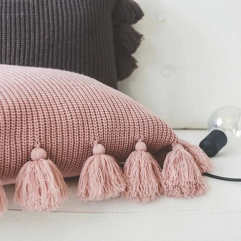 A soft pink knit cushion cover with fluffy tassels, ideal as a decorbites knit cushion for living room decor